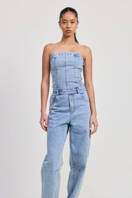 Woman wearing a light blue denim strapless jumpsuit on a white background